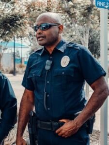 A police officer in uniform standing outdoors, holding a radio, and ensuring public safety.